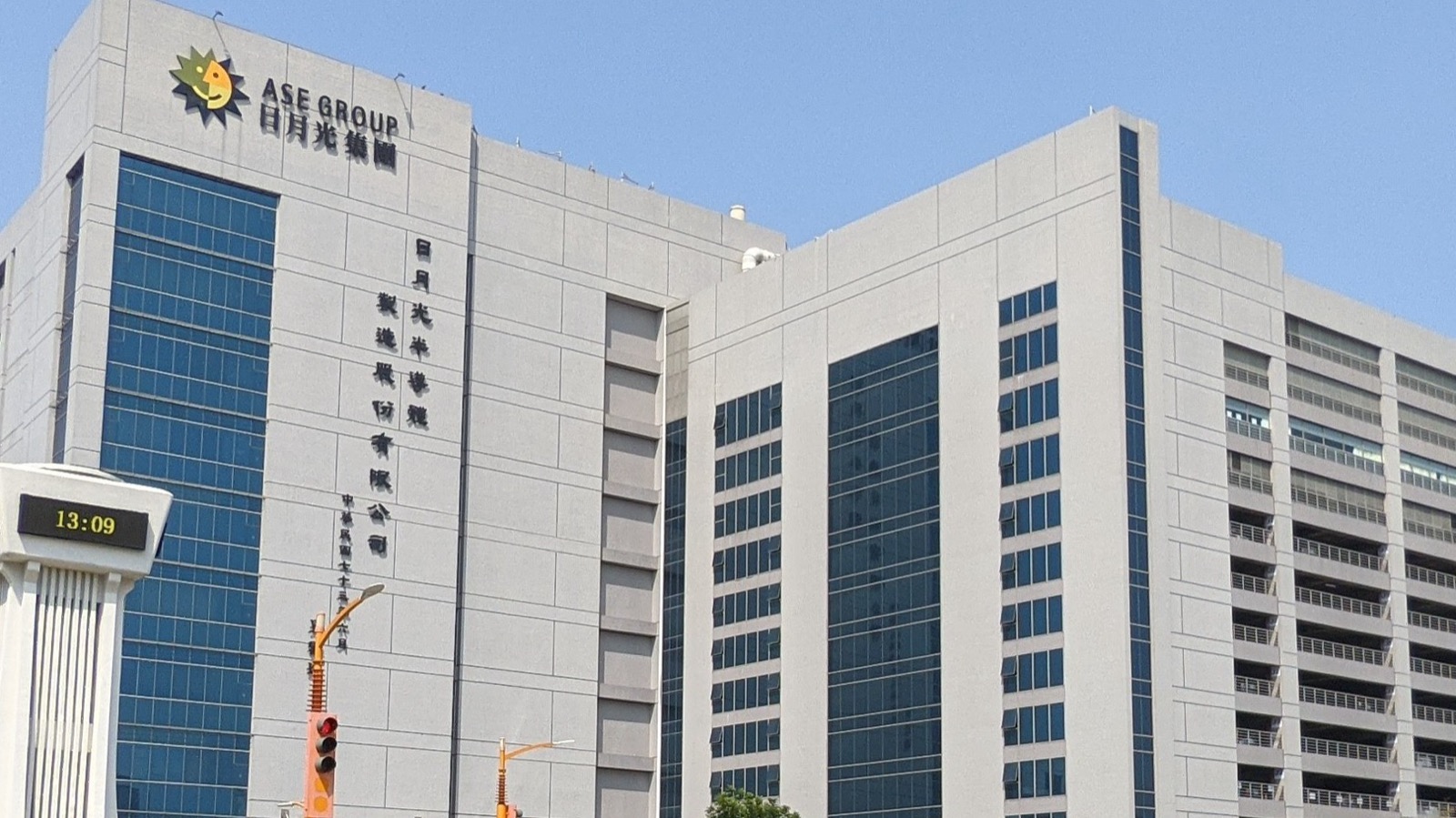 台湾・高雄の楠梓テクノロジー工業団地にある ASE Technology Holding(日月光集団)本社。屋上の「ASE GROUP 日月光集團」ロゴと太陽マスコット、外壁の縦書き社名「日月光半導體製造股份有限公司」で同社と識別できる。手前は敷地内の時計塔。