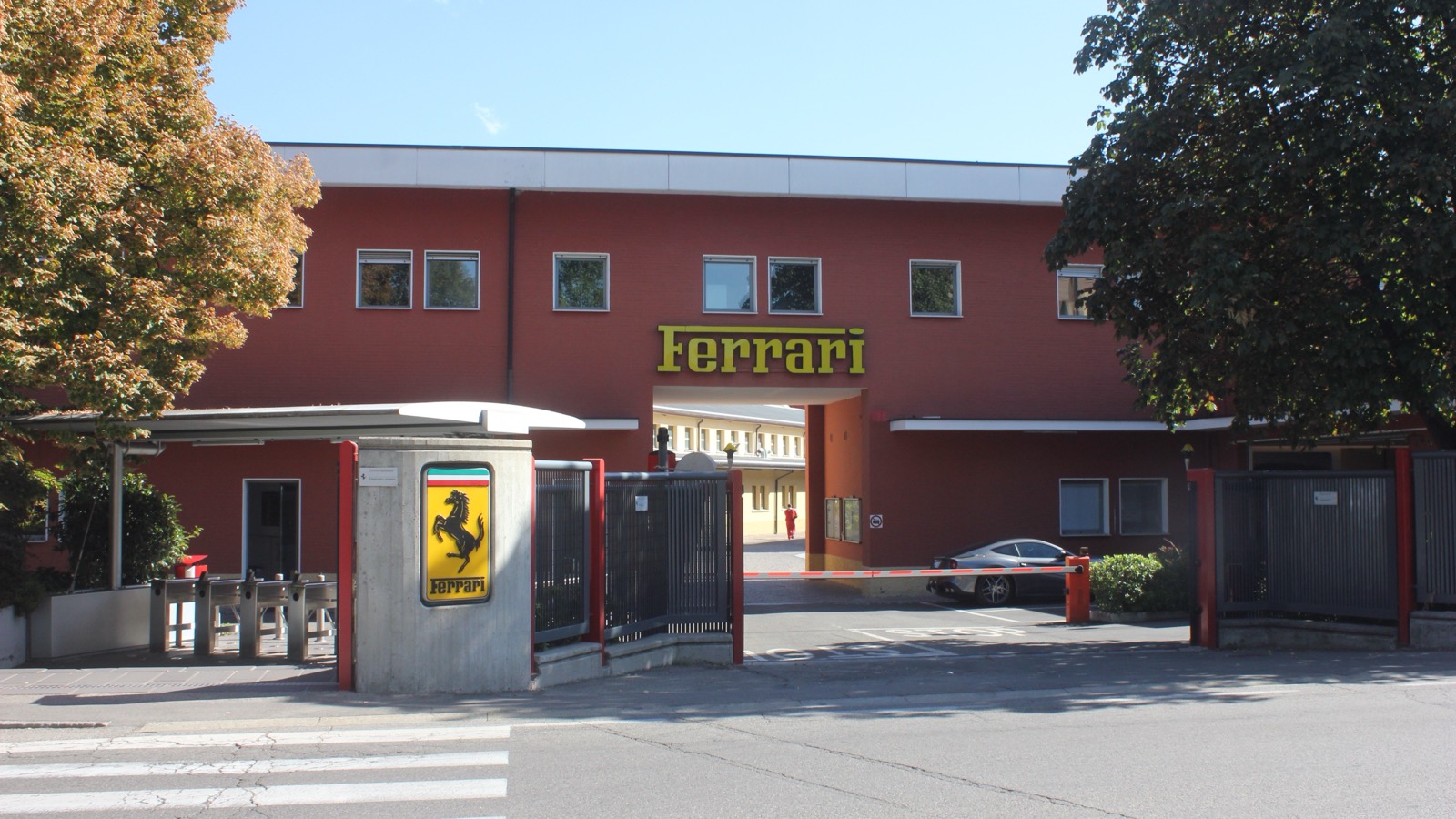 イタリア・マラネッロにあるフェラーリ本社工場の正門。入口アーチ上の黄色い「Ferrari」ロゴと、ゲート脇の跳ね馬(カヴァリーノ・ランパンテ)の看板で一目でフェラーリと分かる。