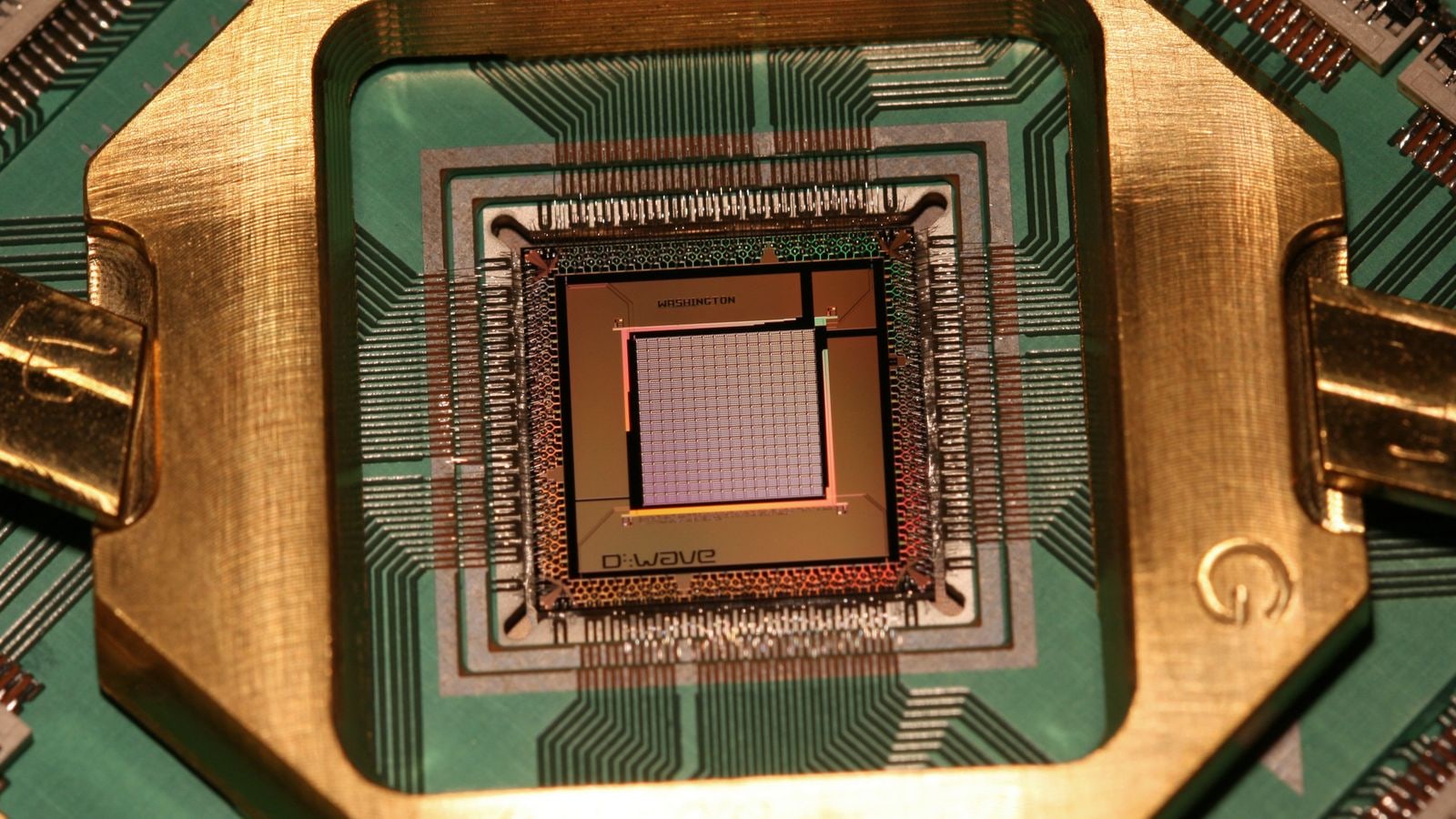 金色の台に据えられたディーウェーブの量子アニーリング用チップ。チップ面にD-Waveの文字が読める